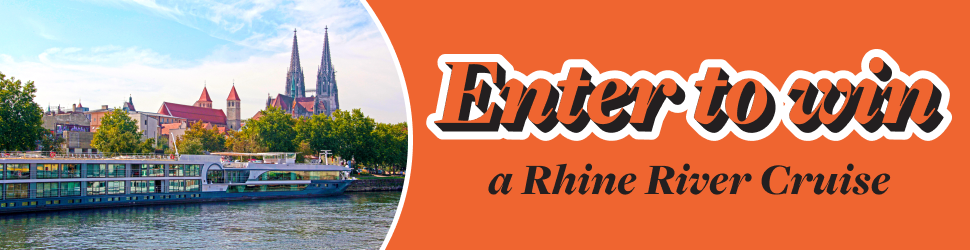 A mid-size cruise ship on a river going by an old European town. Enter to win a Rhine River Cruise.